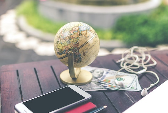 table with a small globe, smartphone, and U.S. dollar bills on it