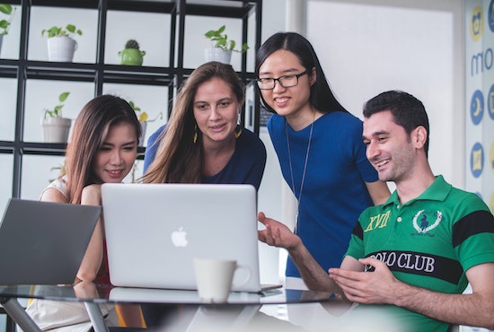 4 university students gathered around a laptop, talking